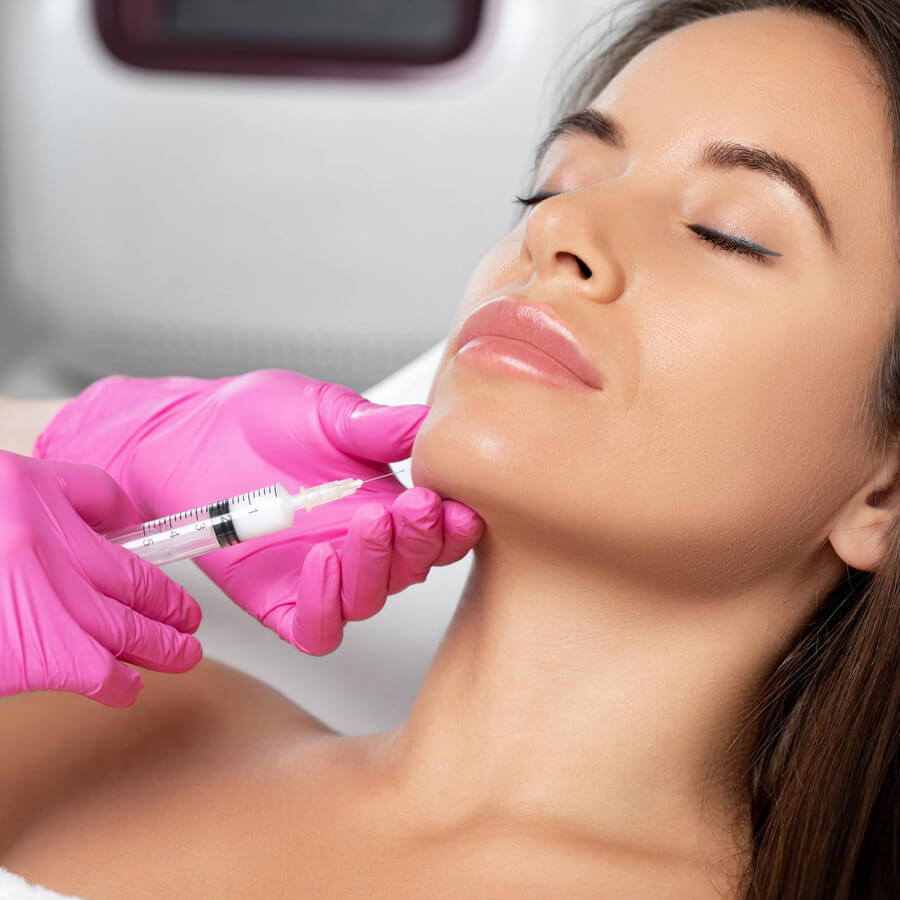 Aesthetic nurse injects filler into a woman's chin.