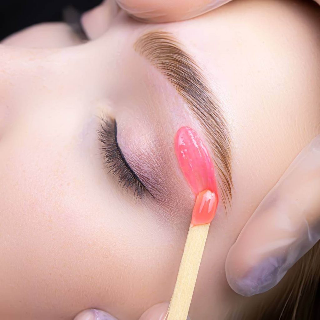 Aesthetician waxes a client's eyebrows.