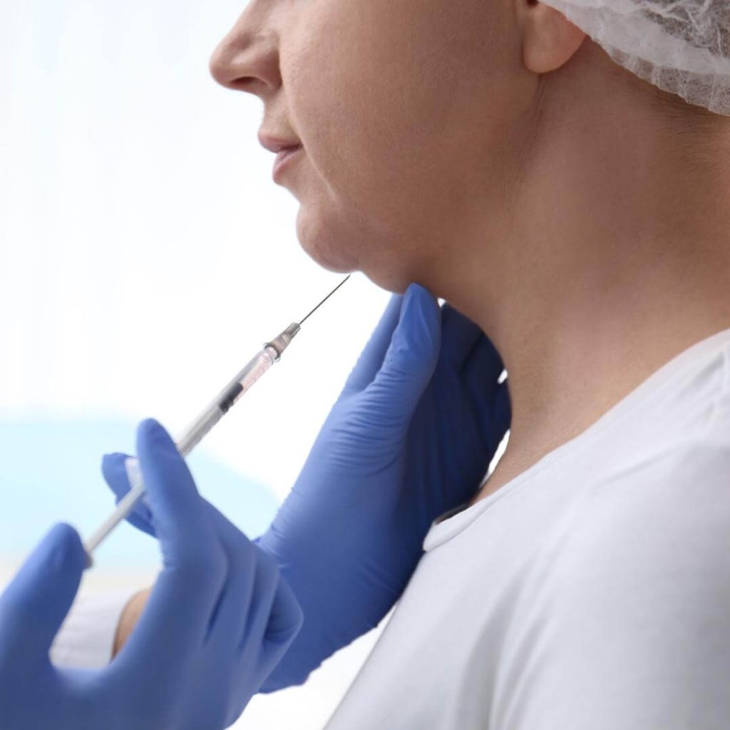 Aesthetic nurse injects fat dissolver under a woman's chin.