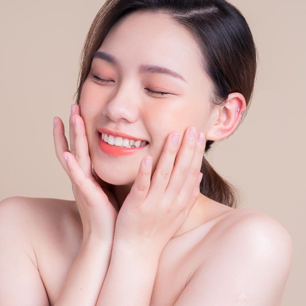 Woman smiles while holding her hands up to her face.